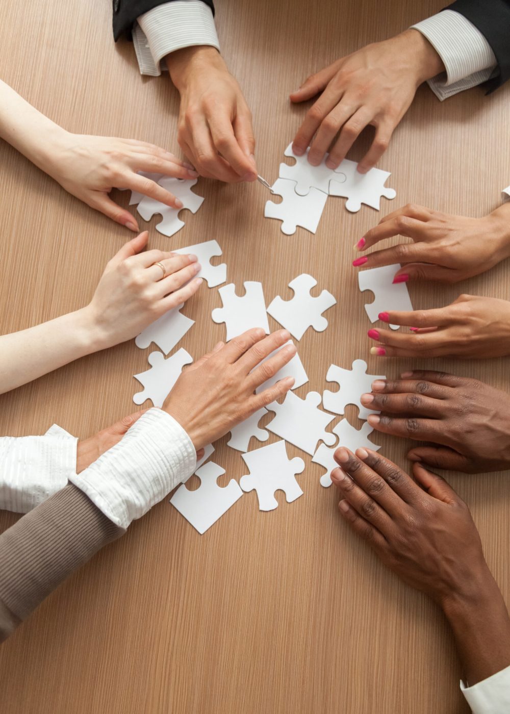 Multiracial team assembling puzzle together, hands of diverse people connecting pieces engaging in finding solutions, teambuilding and teamwork concept, business help support, close up vertical view