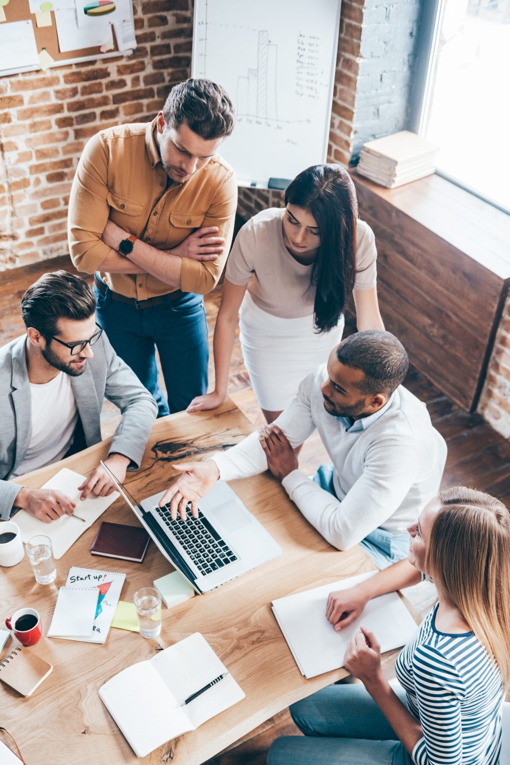 Top view of group of five young people discuss something and gesturing while leaning to the table in office